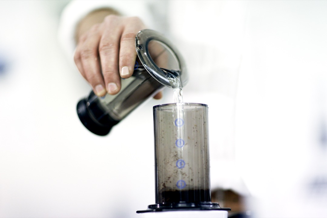 Hand pouring hot water from a kettle into an AeroPress coffee brewer