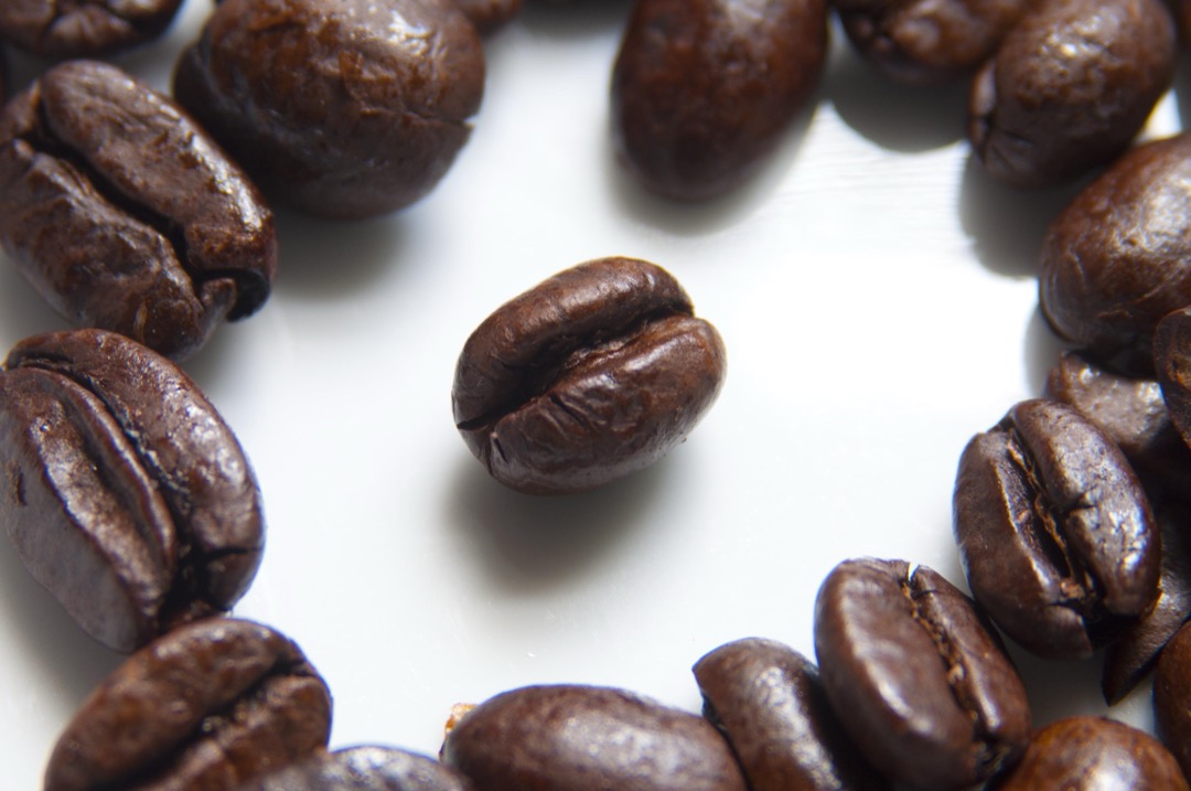 Macro photograph of roasted coffee beans on a white surface with one bean isolated in the center