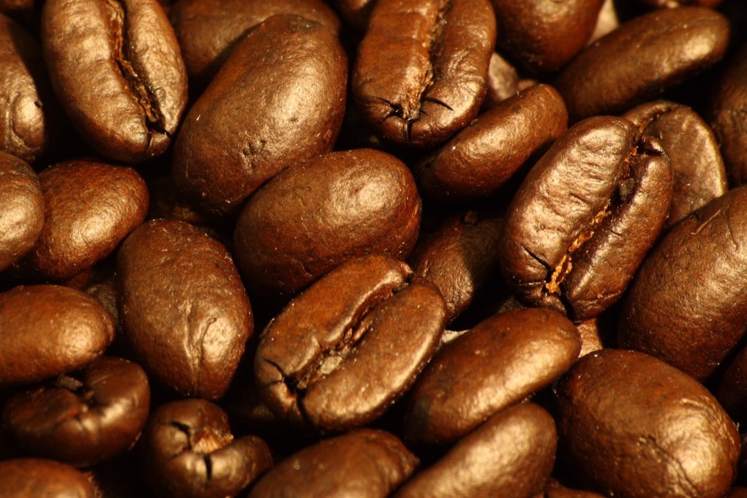 Freshly ground espresso beans in a portafilter beside whole roasted coffee beans