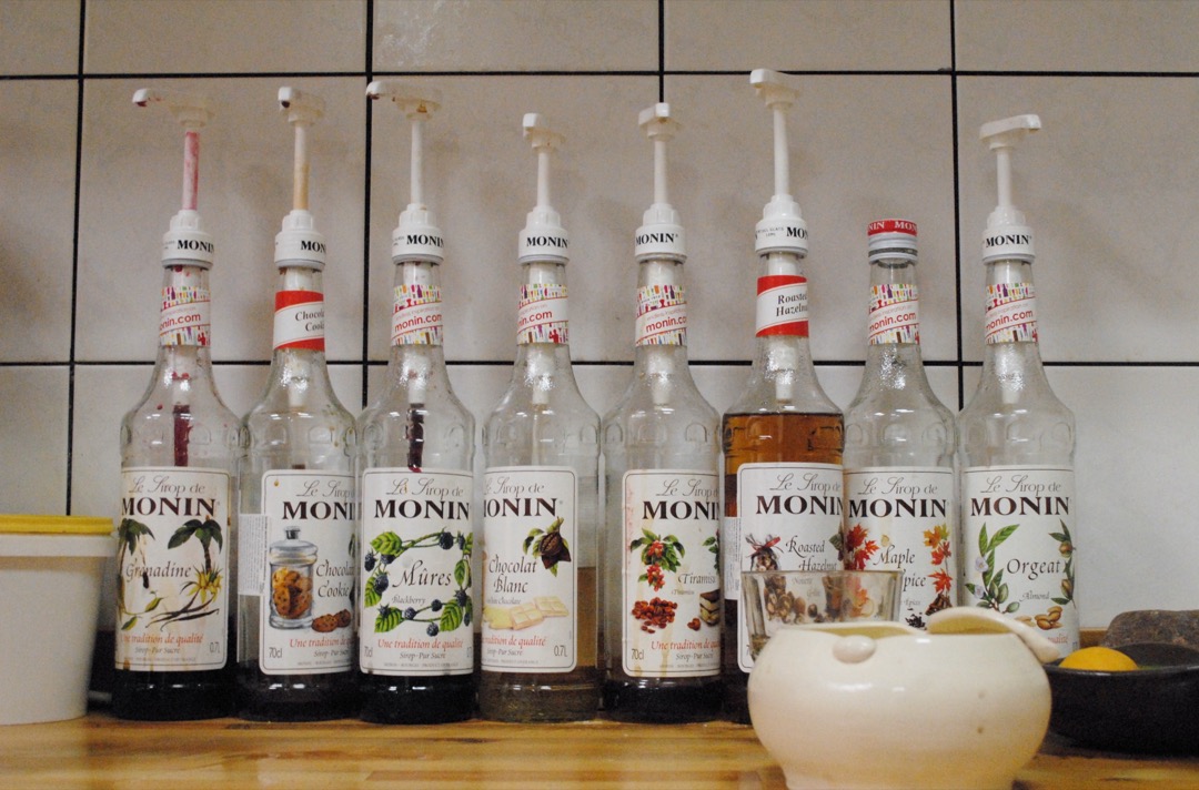 A row of Monin flavoring syrup bottles with pour pumps on a cafe counter