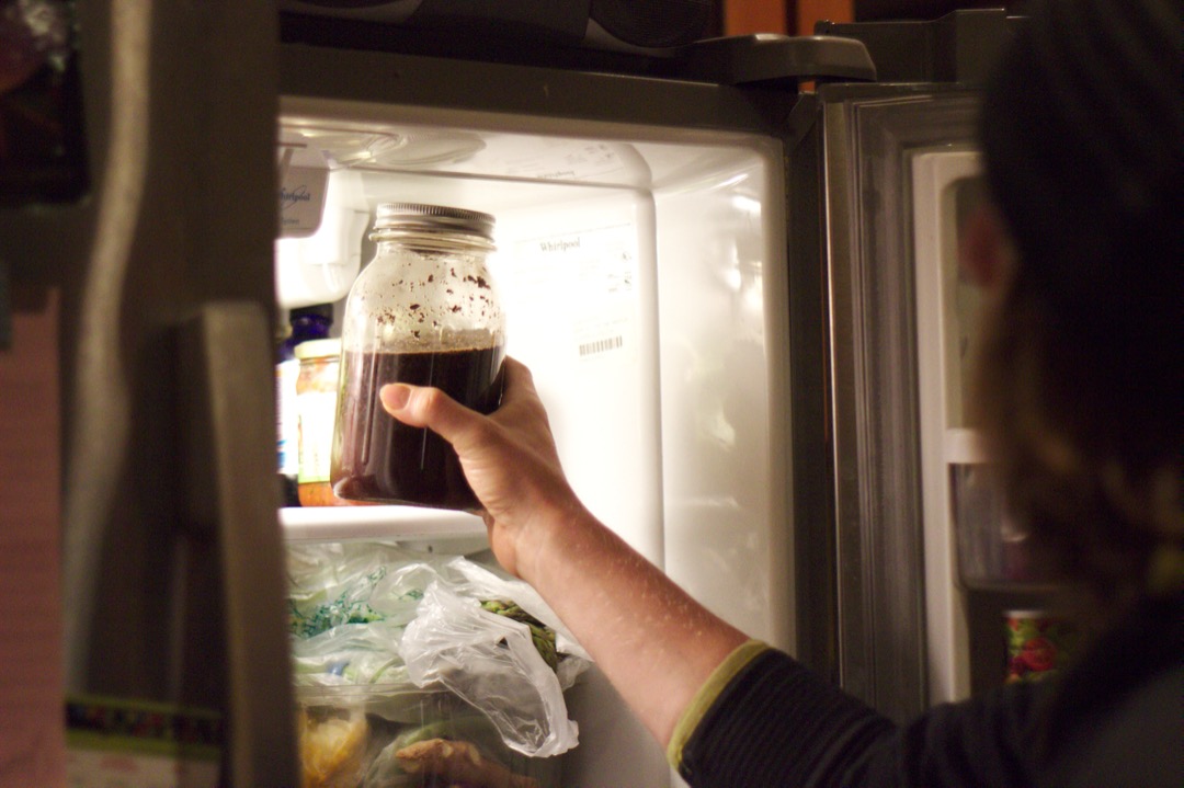 A wide-mouth glass mason jar of finished cold brew coffee being placed on a refrigerator shelf to steep