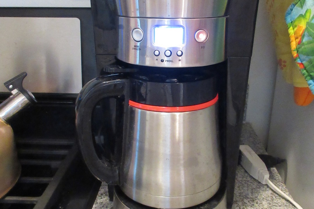 A drip coffee maker brewing a full pot of coffee into a carafe on a kitchen counter