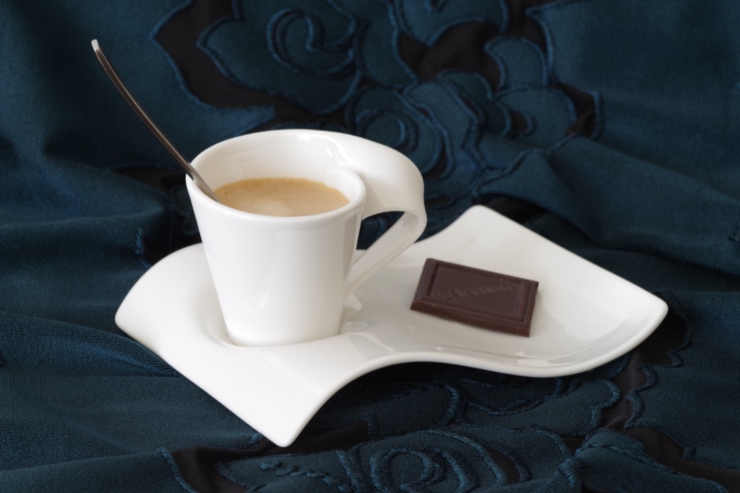 A white porcelain espresso cup of freshly pulled espresso with a layer of crema, resting on a curved white saucer