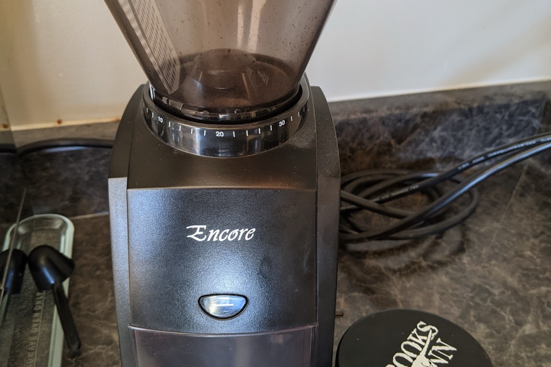 A conical burr espresso grinder beside freshly roasted coffee beans on a kitchen counter