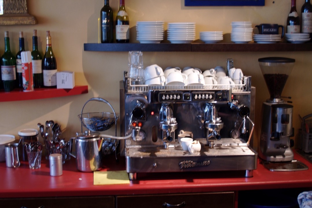 A semi-automatic espresso machine pulling a shot into a glass on a kitchen counter