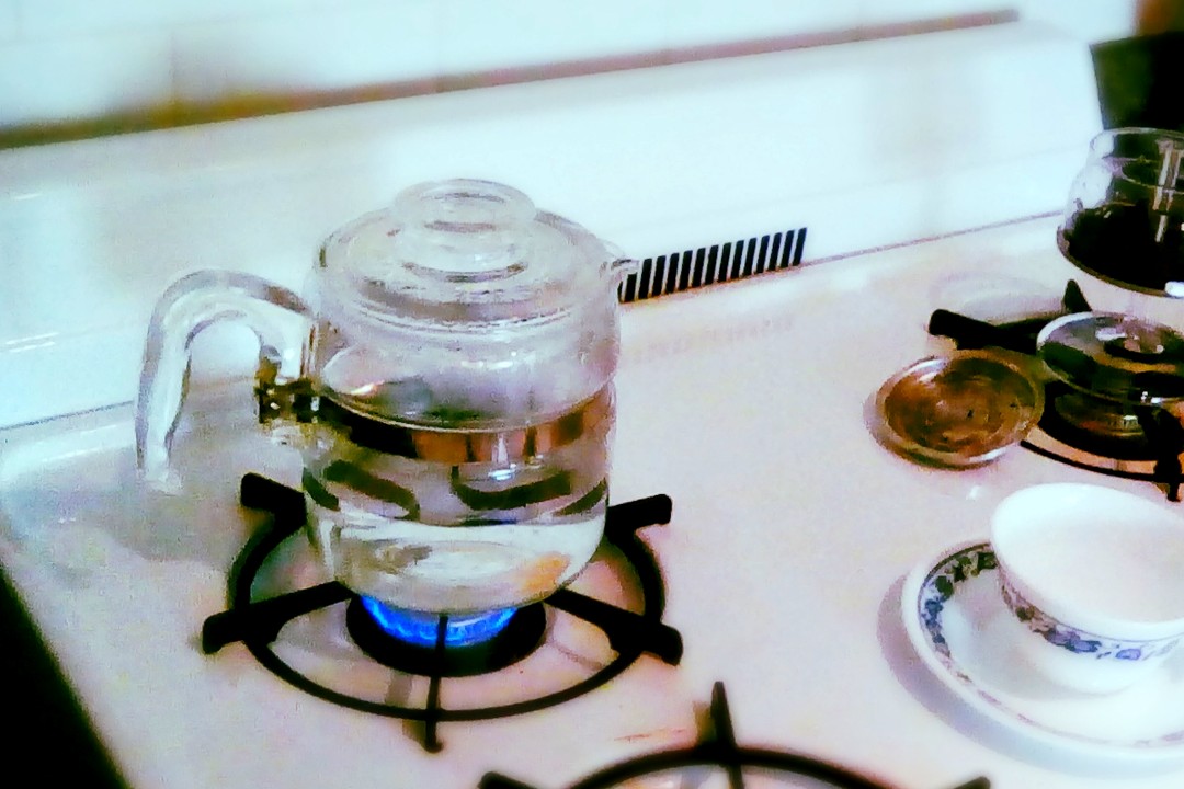 A glass stovetop coffee percolator brewing over a gas flame
