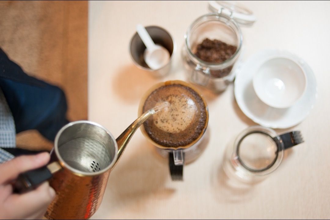A manual pour-over dripper with a paper filter brewing coffee into a glass carafe on a kitchen counter