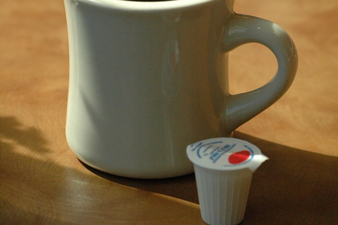 A white diner mug of black coffee beside a single-serve liquid coffee creamer cup