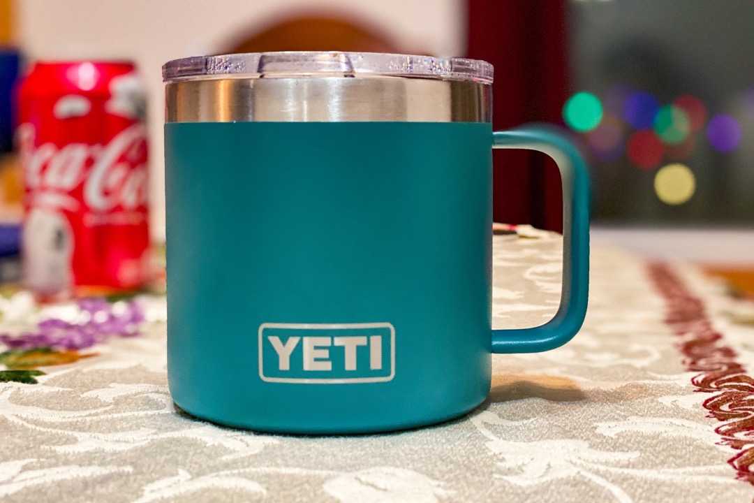 A teal double-wall stainless steel travel coffee mug with a handle and a clear lid on a table