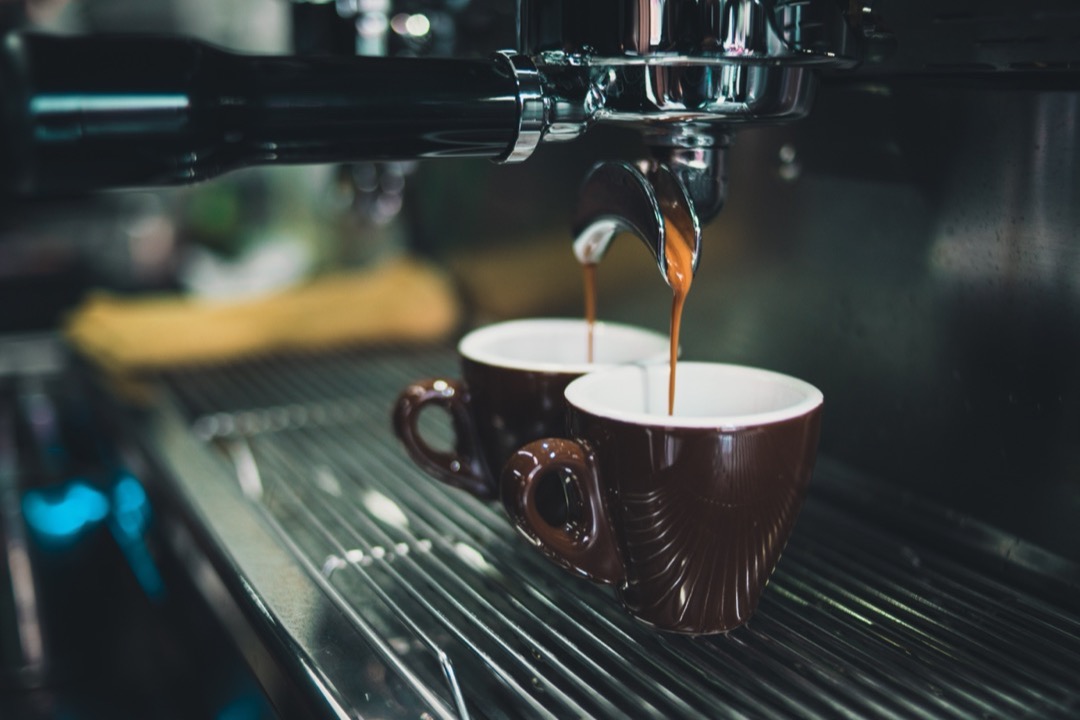 Close-up of an espresso machine brewing into two brown coffee cups