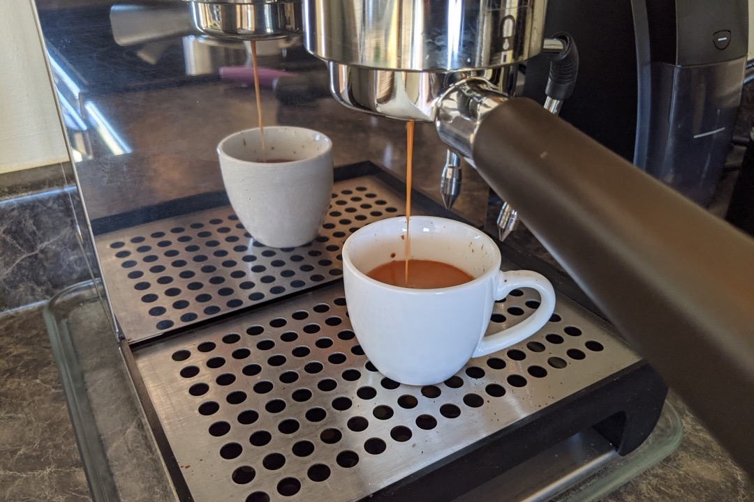 A double espresso shot with thick golden crema pulled from a naked portafilter into a glass