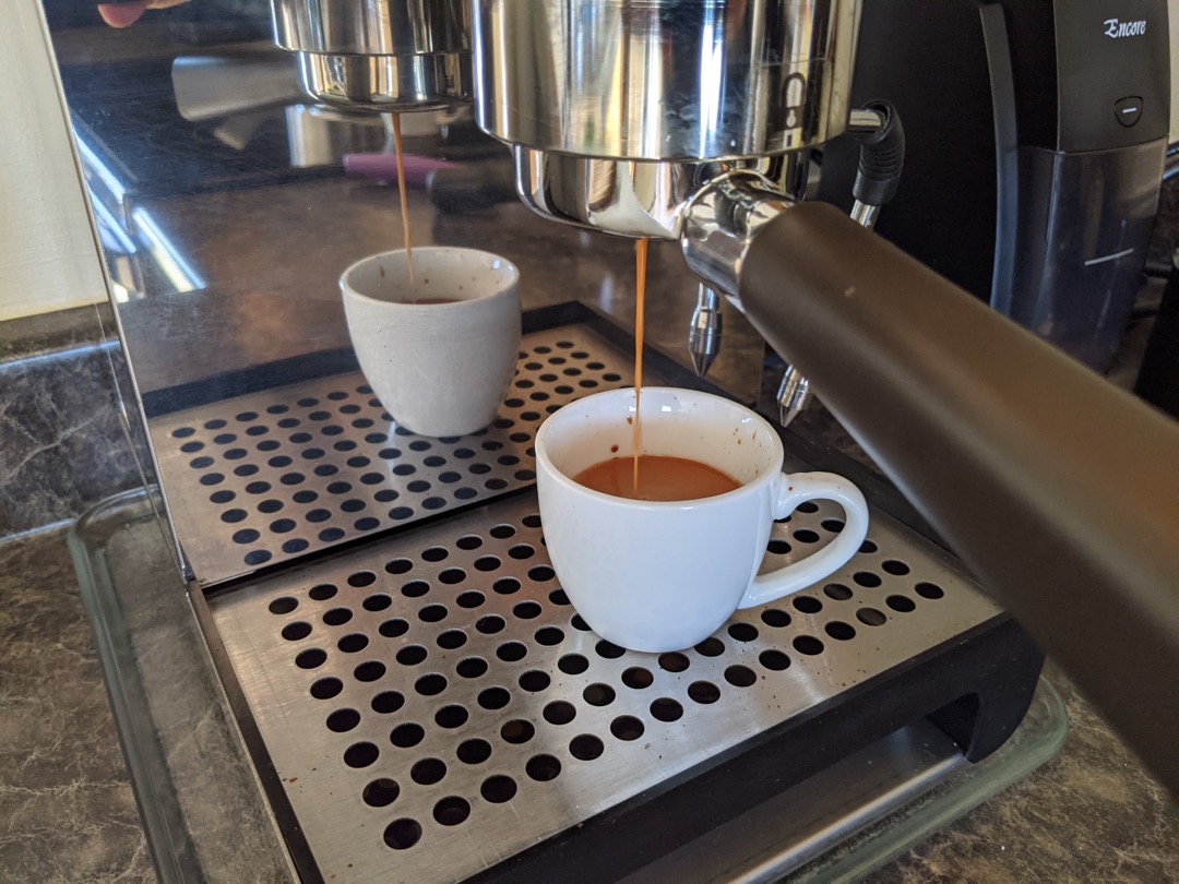 Espresso pulling from a bottomless portafilter into a white cup on a home espresso machine drip tray